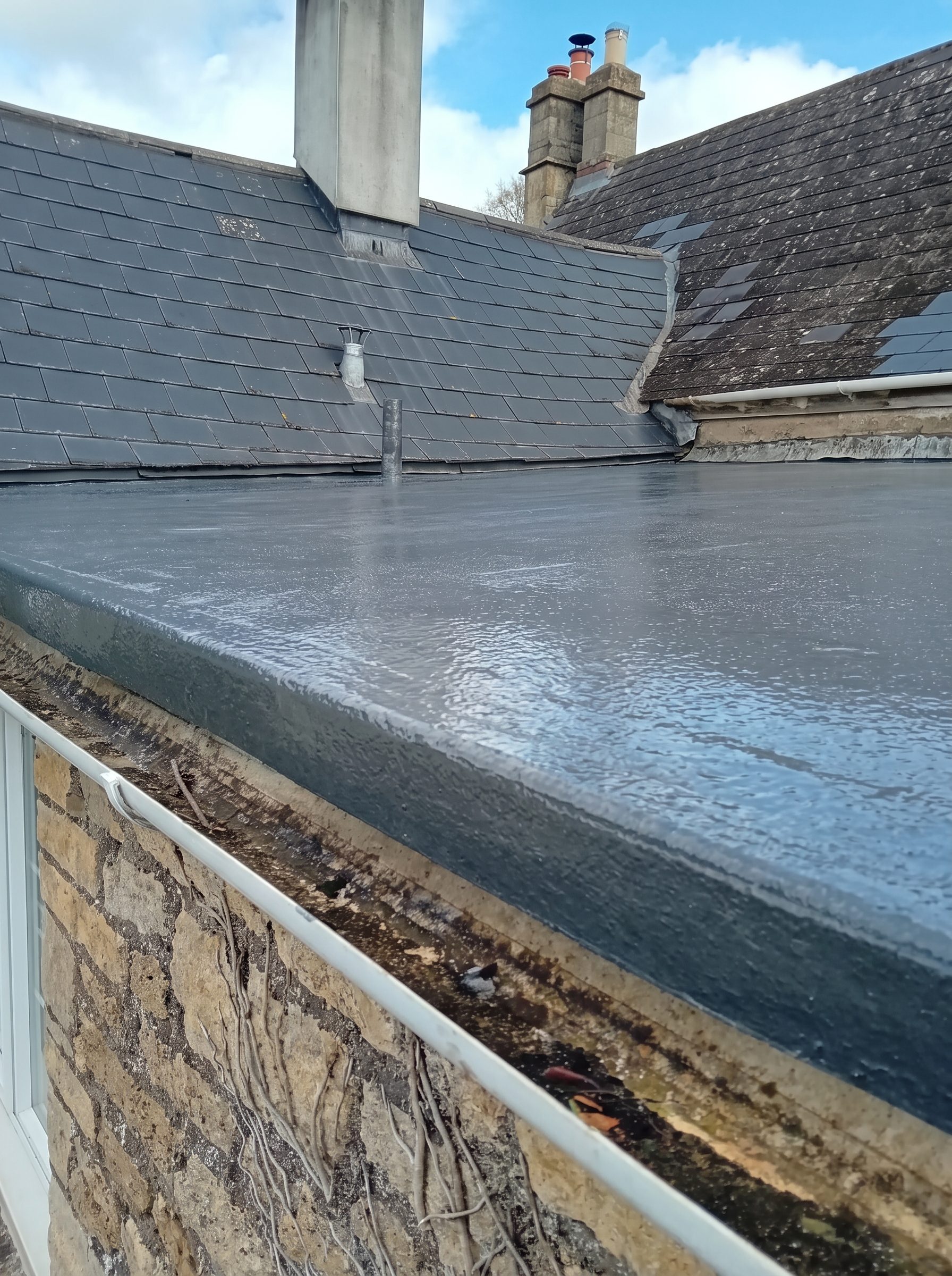 Finished flat roof meeting a slate pitched roof and chimney stack